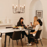 Three women sit around a marble dining table, enjoying wine and a charcuterie board in a modern, elegantly decorated room with warm lighting and minimalist decor.
