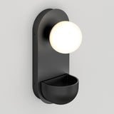 A modern black wall sconce with a round, frosted white globe light at the top and a small, bowl-shaped compartment at the bottom, mounted on a light gray wall.