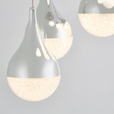 Close-up of three modern pendant lights with a teardrop shape, silver tops, and textured frosted bottoms emitting a warm glow, set against a light gray background.