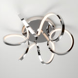 A modern ceiling light fixture with intertwined chrome loops and integrated LED strips, mounted on a circular base, casting soft light and intricate shadows on the white ceiling.