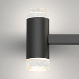 A modern wall-mounted black sconce light with cylindrical frosted glass ends featuring bubble-like patterns, illuminating both upward and downward against a plain light-colored wall.