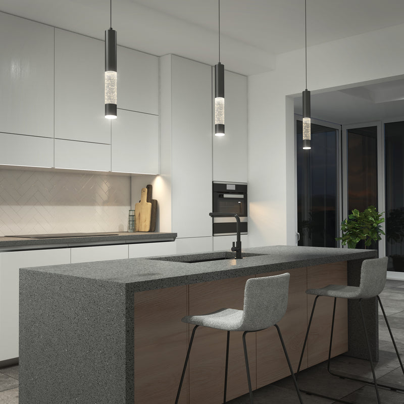 Modern kitchen with a gray stone island, two bar stools, built-in cabinets, a built-in oven, a sink with a black faucet, a plant near large windows, and Mist LED pendant lights by Artika hanging above.