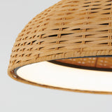 Close-up of a woven rattan lampshade with a dome shape, showing detailed texture and natural color. The light inside creates a warm, soft glow against the neutral background.