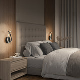 A modern bedroom with a tufted headboard, neatly made bed with gray and white bedding, wooden nightstands, a cup on one nightstand, decorative pillows, and unique wall sconces on either side of the bed.