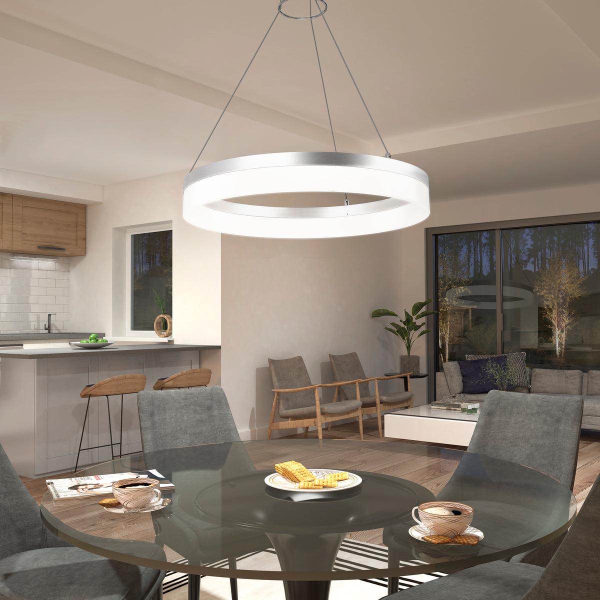 A modern dining area with a round glass table set for breakfast, gray upholstered chairs, a glowing circular pendant light above, and an open view of a cozy living room and kitchen in the background.