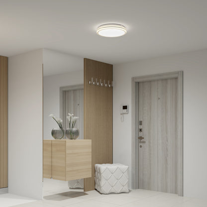 A modern hallway with light wood and white decor, featuring a light wood door, a floating cabinet with two glass vases of white flowers, a quilted white ottoman, and a wall mirror.