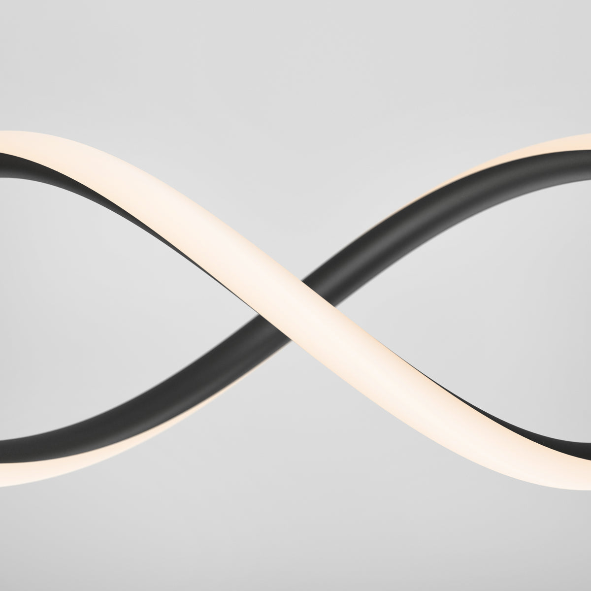A modern light fixture with two intertwined, looping bands—one black and one illuminated white—set against a plain light gray background, forming an infinity symbol shape.