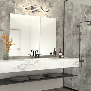 Modern bathroom with a marble countertop, double black faucets, large mirror illuminated by the Artika Swirl modern LED bathroom vanity light, decorative orange flowers in a vase, toiletries, gray towels, and glass shower with matte black fixtures.