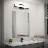 A modern bathroom with a rectangular mirror, a black faucet, a soap dispenser, a small potted plant, and a rectangular LED light fixture above the mirror. A window and folded towels are seen on the right.