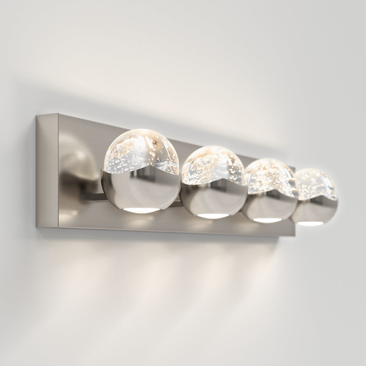 A modern wall-mounted light fixture with four round glass bulbs set on a rectangular metal base, emitting a soft, bright light against a white wall.