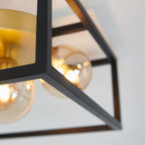 Close-up of a modern ceiling light fixture with exposed bulbs, featuring a black metal geometric frame and gold accents, mounted on a white ceiling.