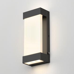 The Artika Glacier indoor-outdoor LED wall light features a matte black frame and frosted white diffuser, mounted on a light gray wall, casting soft up-and-down lighting with its modern rectangular design.