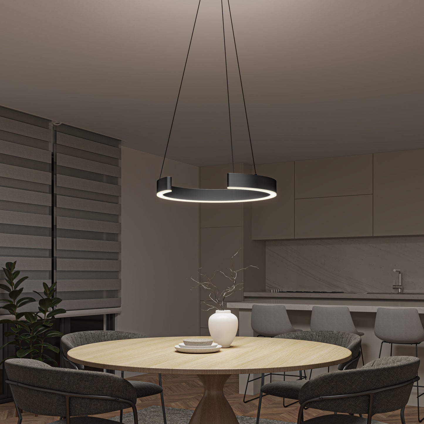A modern dining area features a round wooden table, four gray chairs, a white vase with branches, and the Artika-CAN-dev Vance modern LED pendant light 3 CCT overhead. A minimalist kitchen and striped blinds complete the refined design.