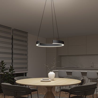 A modern dining area features a round wooden table, four gray chairs, a white vase with branches, and the Artika-CAN-dev Vance modern LED pendant light 3 CCT overhead. A minimalist kitchen and striped blinds complete the refined design.