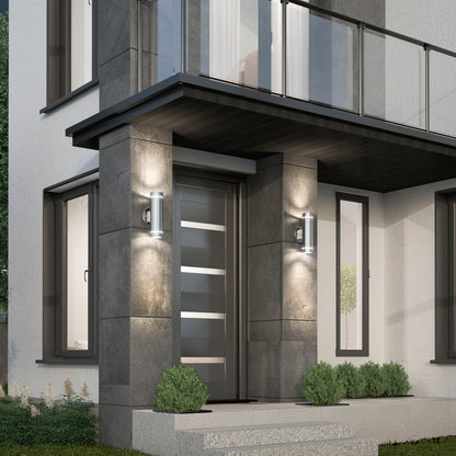 Modern house entrance with a sleek dark front door featuring horizontal glass panels, flanked by two Artika C7 indoor-outdoor wall lights. The exterior walls are gray with large windows and small green bushes by the steps.