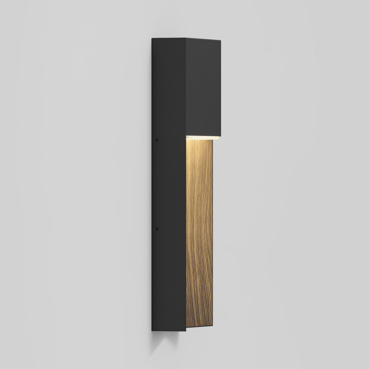 A modern wall sconce with a rectangular black metal body and a vertical wooden panel, emitting a soft light downward. The fixture is mounted on a plain light gray wall.