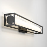 A modern wall sconce with a rectangular black metal frame and a cylindrical white light fixture, mounted on a smooth, light-colored wall.