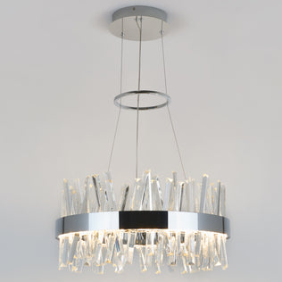 The Artika Enchanted LED pendant light features a circular chrome frame suspended by cables, with irregular clear glass prisms that emit soft white light, creating a modern look against any white ceiling.