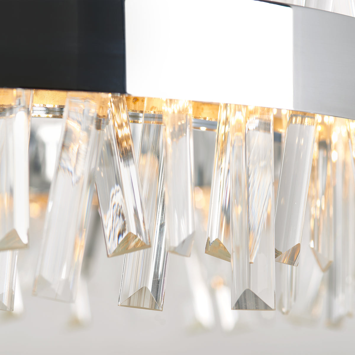Close-up of a modern chandelier with hanging, angular crystal prisms reflecting warm light. The crystals are suspended from a metallic circular frame, creating a sparkling and elegant effect.