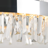 Close-up of a modern chandelier with hanging, angular crystal prisms reflecting warm light. The crystals are suspended from a metallic circular frame, creating a sparkling and elegant effect.