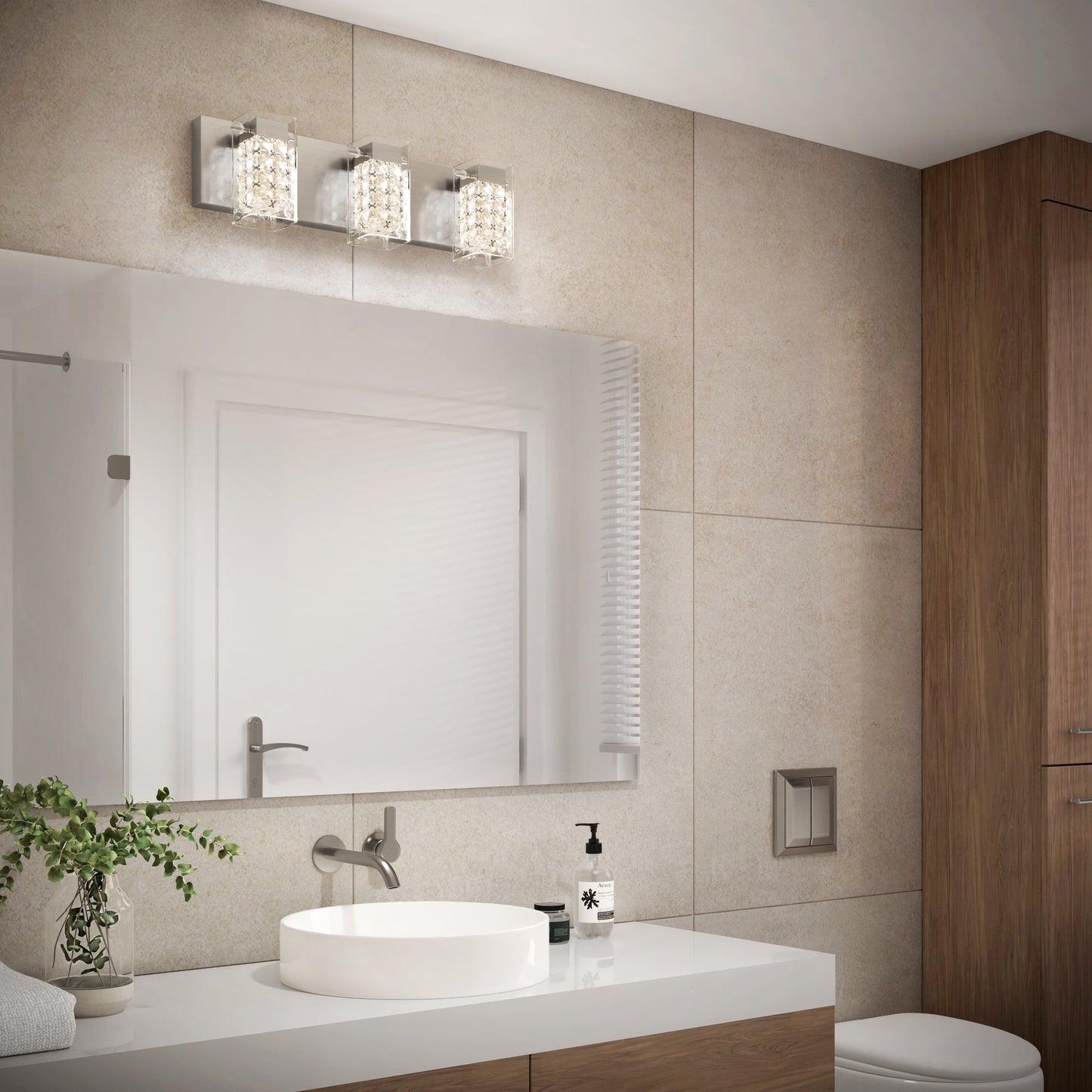 Modern bathroom with beige tiled walls, large mirror, round white sink on a wooden vanity, potted plant, soap dispenser, and Artika Crystal Cube LED bathroom vanity light 5 CCT above the mirror. A white door is reflected.