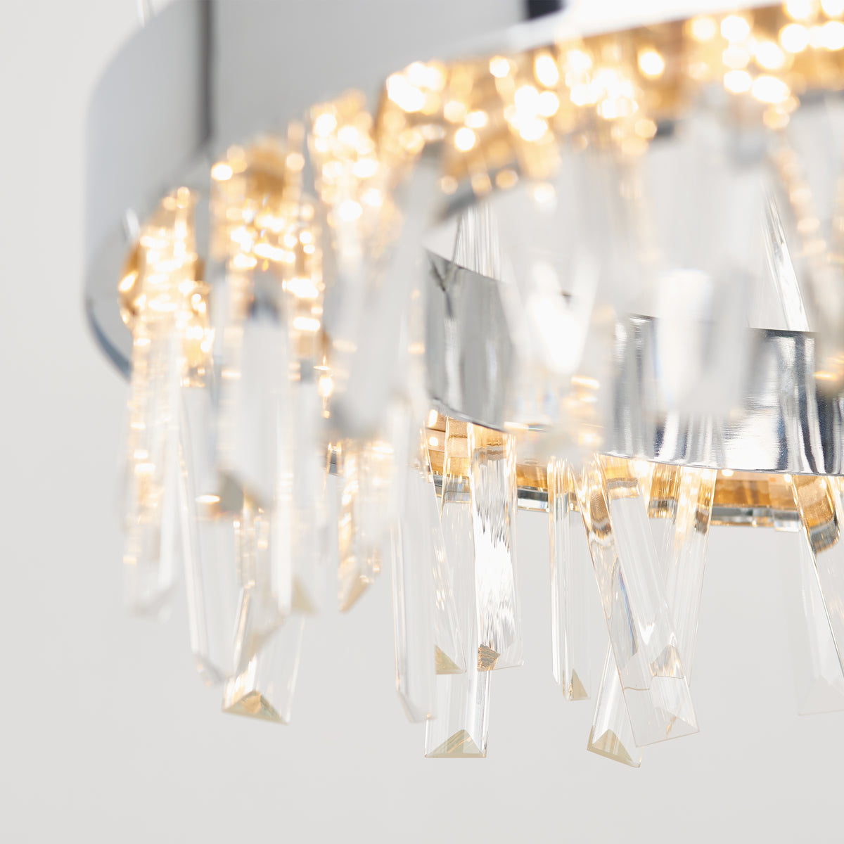 Close-up of a modern chandelier with a chrome finish, featuring hanging crystal prisms and warm glowing lights, creating a sparkling and elegant effect.