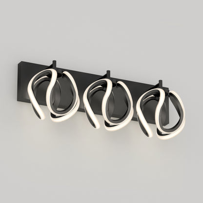 A modern wall-mounted light fixture with three abstract, looped LED lights attached to a rectangular black base against a light gray wall.