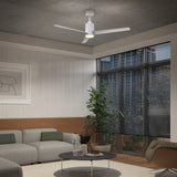 A modern living room with a gray sectional sofa, a round black coffee table, a potted plant, wall art, large windows with blinds, and a white ceiling fan with a light.