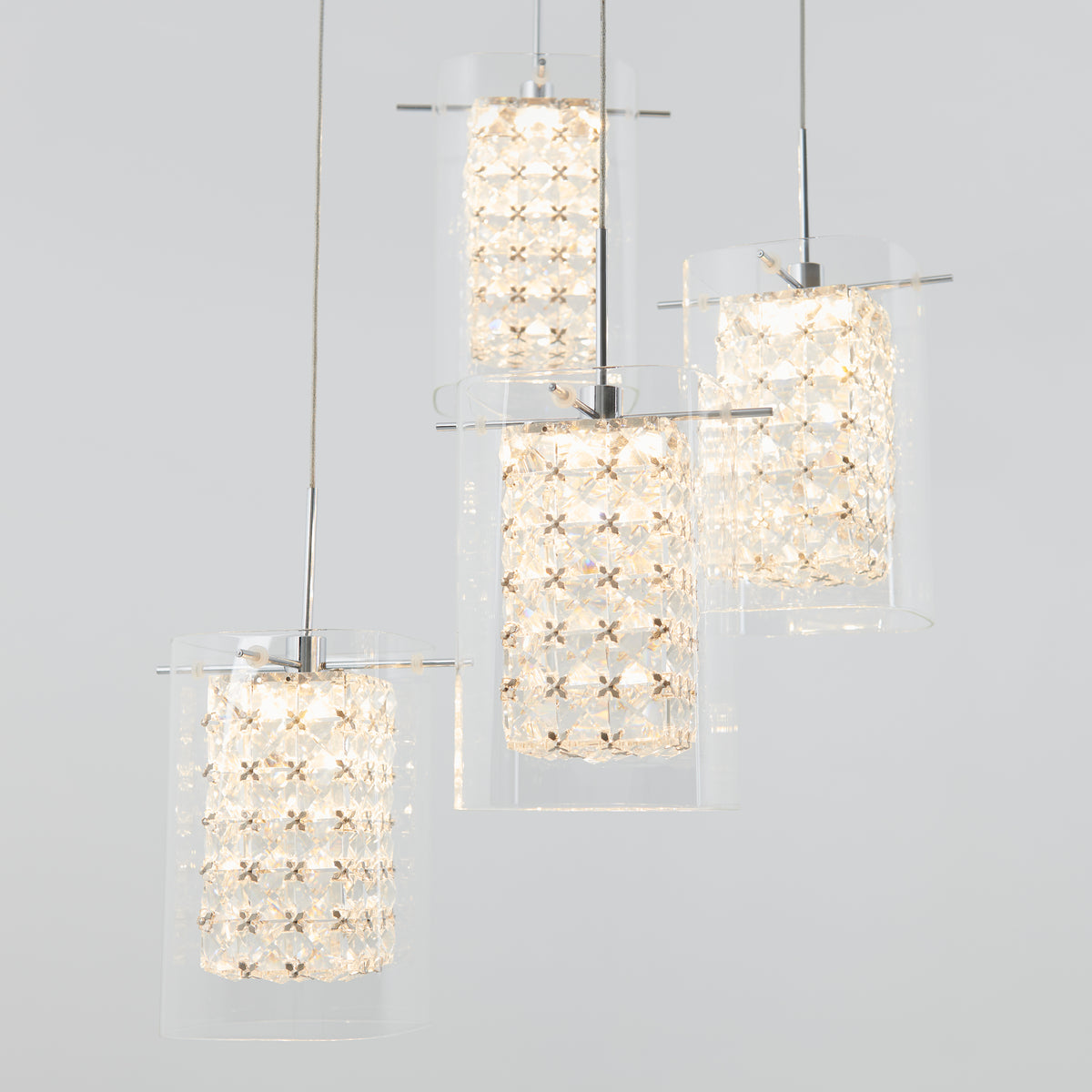Three modern pendant lights with cylindrical glass shades and intricate crystal lattice interiors hang at different heights from the ceiling, emitting a soft, bright glow against a plain light gray background.
