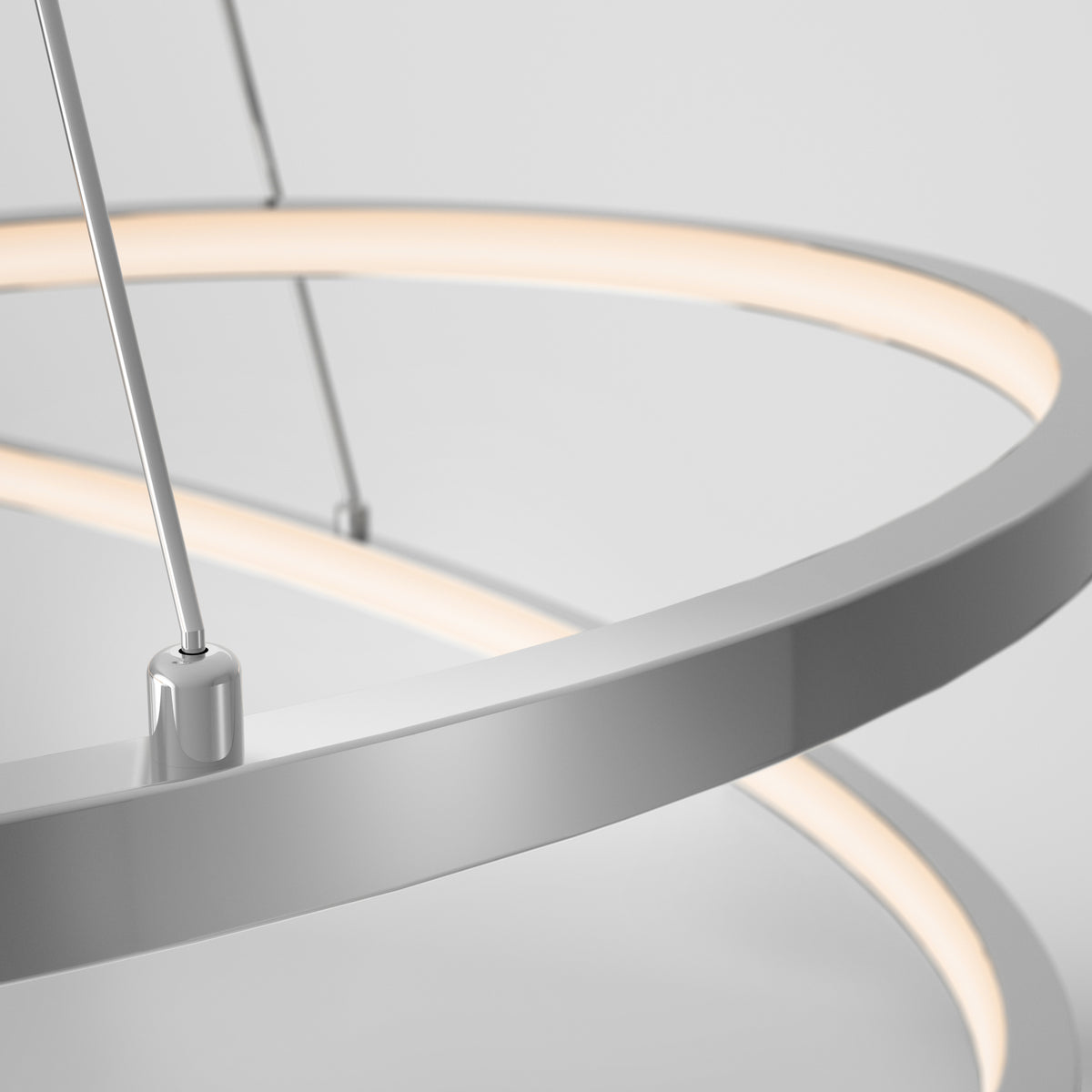 Close-up of a modern, circular LED pendant light with a sleek metallic frame, suspended by thin wires against a plain white background. The light emits a soft, warm glow.
