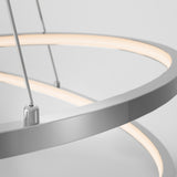 Close-up of a modern, circular LED pendant light with a sleek metallic frame, suspended by thin wires against a plain white background. The light emits a soft, warm glow.