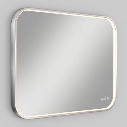 The Artika Royce dimmable LED mirror 3 CCT is a rectangular, wall-mounted mirror with rounded corners and an LED light strip around the edge, featuring three touch controls in the bottom right corner against a plain gray wall.