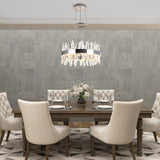 A modern dining room with a dark wood table, six beige upholstered chairs, a glass vase with white flowers, place settings, and a contemporary chandelier hanging above on a gray textured wall.