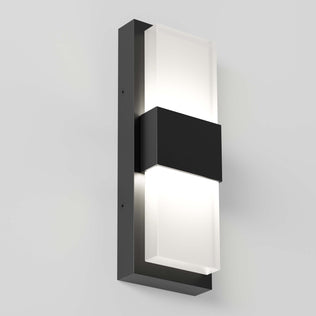 The Artika Mazza Frosted indoor-outdoor LED wall light features a sleek rectangular black metal frame with two frosted glass panels, casting a soft glow on a light gray wall.