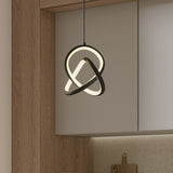 A modern pendant light with a twisted, looped design hangs in a kitchen with wood paneling, pale cabinets, and a speckled countertop. A cutting board rests against the backsplash.