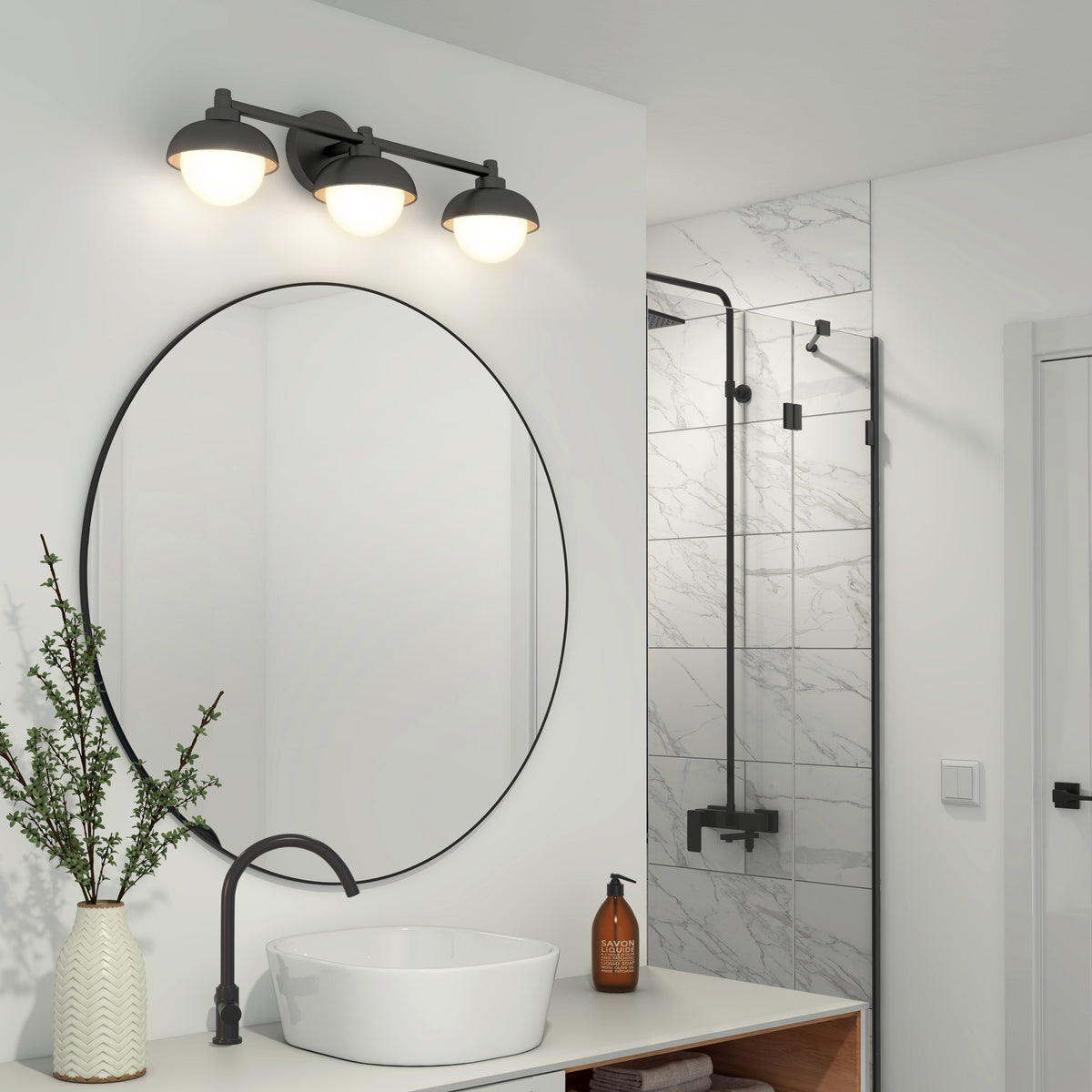 Modern bathroom with a round mirror, white vessel sink, black faucet, and a vase with greenery. Above the mirror is the Artika Boden 27-in Integrated LED 5-CCT Vanity Light Bar. In the background, a shower features white marble tiles and black fixtures.