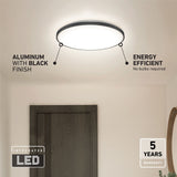 A round ceiling LED light with a black aluminum finish is mounted above a wooden door. Text highlights its energy efficiency, integrated LED, and 5-year warranty. No bulbs are required.