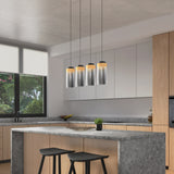 Modern kitchen with light wood cabinets, gray countertops, a large island with two black stools, pendant lights above, a potted plant on the island, and a large window with greenery visible outside.