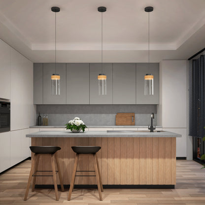 Modern kitchen with a wooden island, two bar stools, and three Artika Hanson 1-light LED pendant lights overhead. White and gray cabinets, built-in oven, vase with white flowers on the island, and dark window blinds.