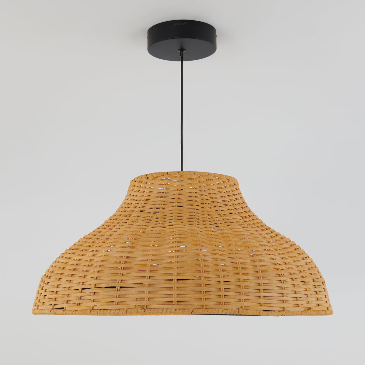 A wicker pendant light with a wide, woven rattan lampshade hangs from the ceiling by a black cord and circular ceiling mount against a plain white background.