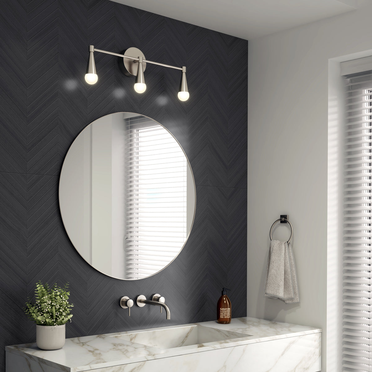A modern bathroom with a round mirror, marble sink, wall-mounted faucet, three-bulb vanity light, potted plant, soap dispenser, towel ring with a gray towel, and a window with white blinds.