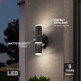 A modern outdoor wall light with a matte black finish emits light from both ends. Text highlights its integrated LED, energy efficiency, no bulbs required, and five-year warranty. The setting is evening.