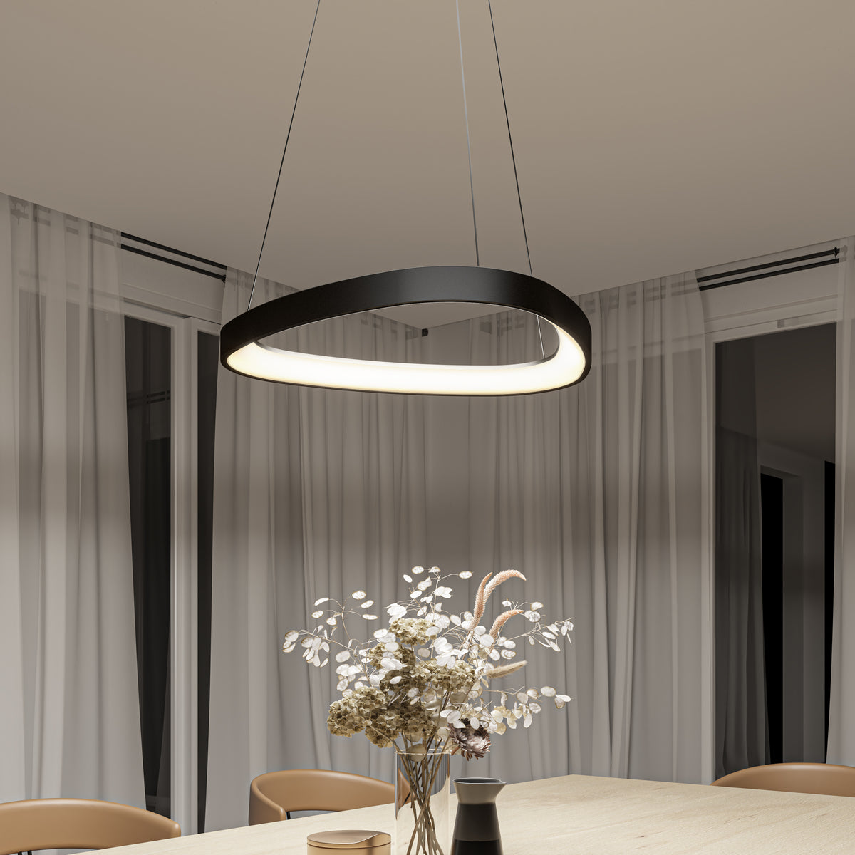 A modern circular pendant light hangs above a wooden dining table with a vase of dried flowers; sheer curtains cover large windows in the background.