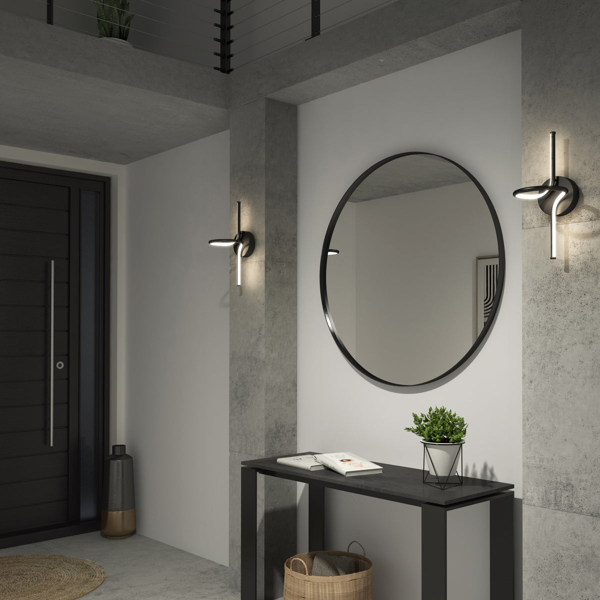 A modern entryway with concrete walls, a round mirror above a black console table, a small potted plant, books, a basket underneath, and sleek wall sconces on either side of the mirror.