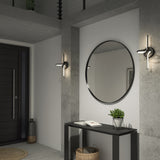 A modern entryway with concrete walls, a round mirror above a black console table, a small potted plant, books, a basket underneath, and sleek wall sconces on either side of the mirror.