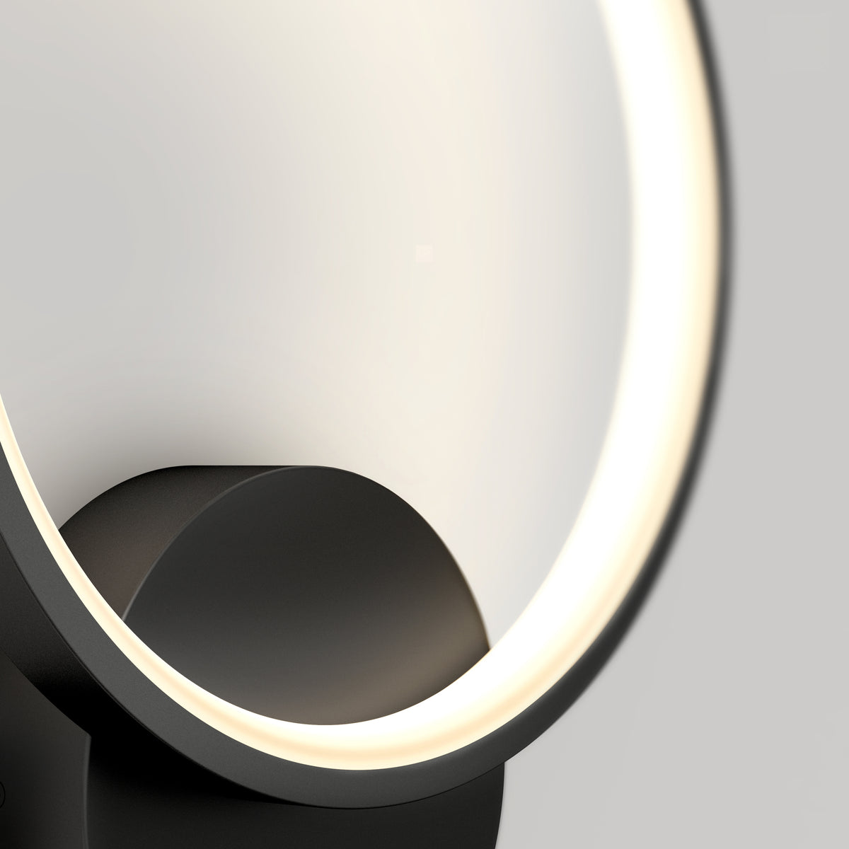 A close-up of a modern, circular LED lamp with a black base and a glowing, white light ring against a light gray background.