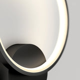 A close-up of a modern, circular LED lamp with a black base and a glowing, white light ring against a light gray background.