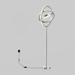 The Artika Pivot modern LED floor lamp 3 CCT, featuring a metallic stand and circular LED design, is plugged into a wall outlet against a plain gray background with its power cord visible on the floor.