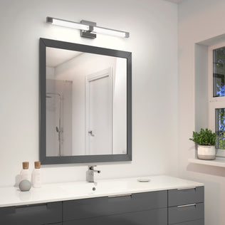 A modern bathroom features a large square mirror over a white countertop with gray drawers. Above, the Artika Tivoli modern LED bathroom vanity light 5 CCT provides sleek illumination, while bottles and a potted plant decorate the space.
