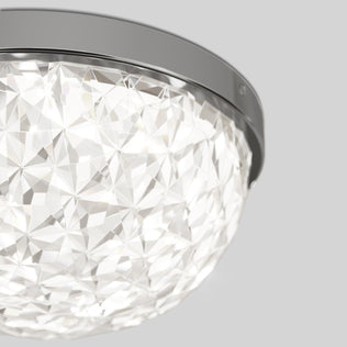 A close-up of Artikas Carat LED flush mount light features a faceted diamond-patterned glass cover and metallic rim, set against a plain light gray background.